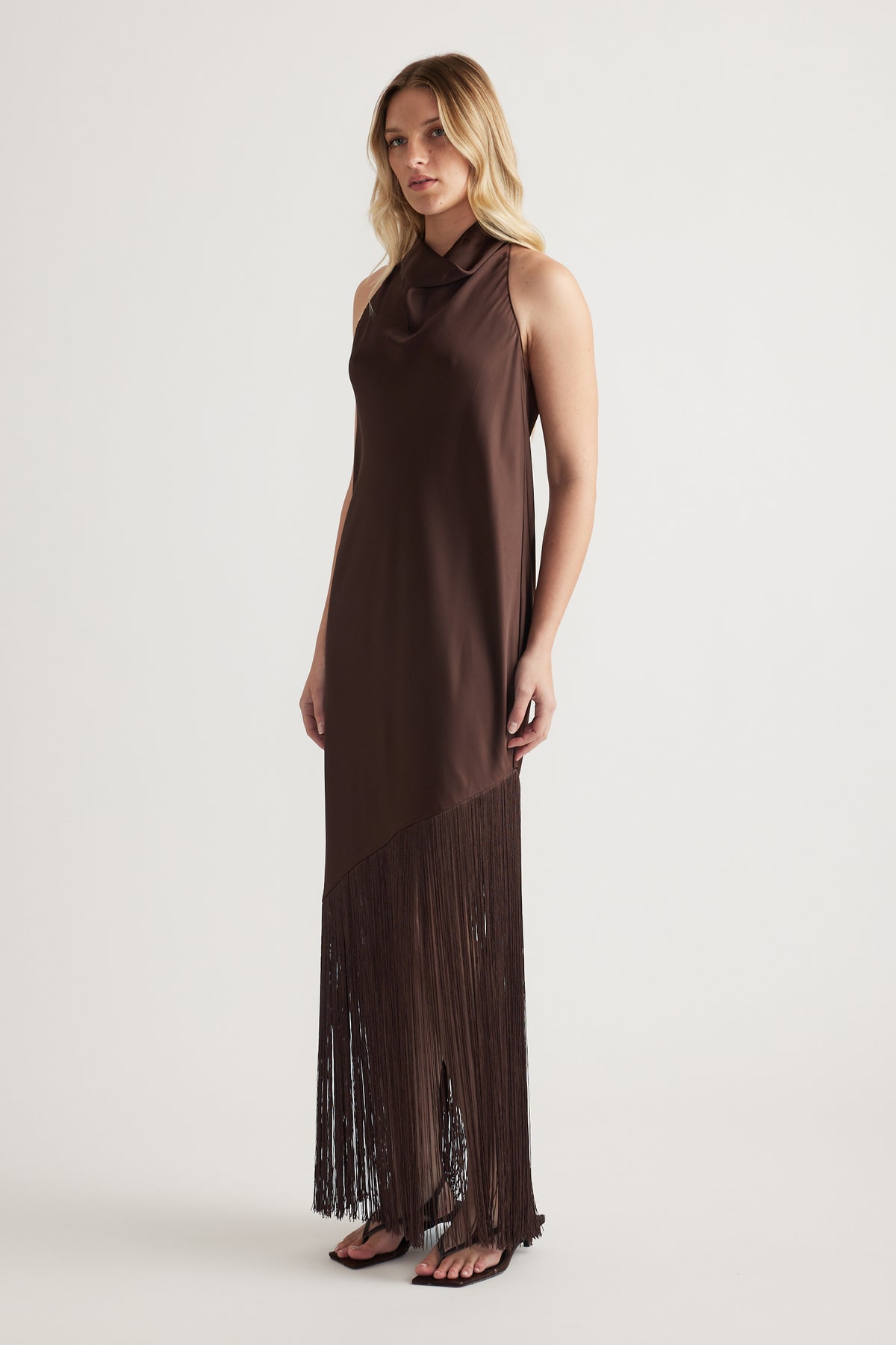 Woman wearing a chocolate brown halter maxi dress with a draped fringe hem