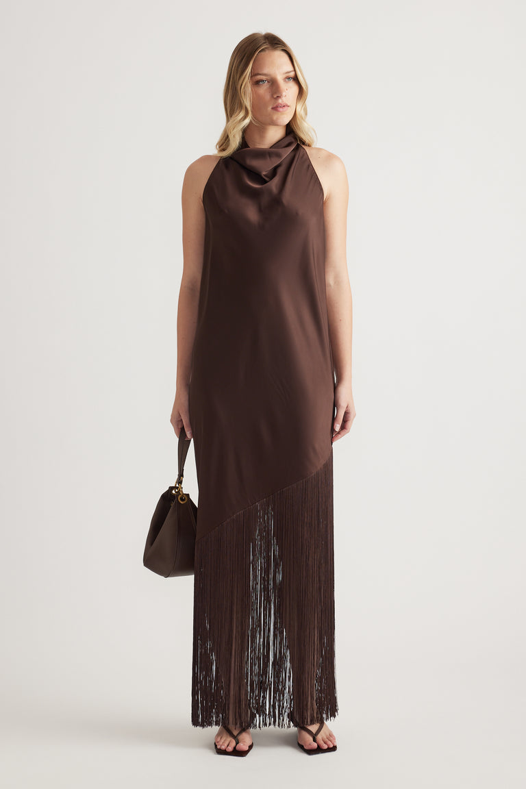 Woman wearing a brown sleeveless halter maxi dress with fringe hem and carrying a handbag