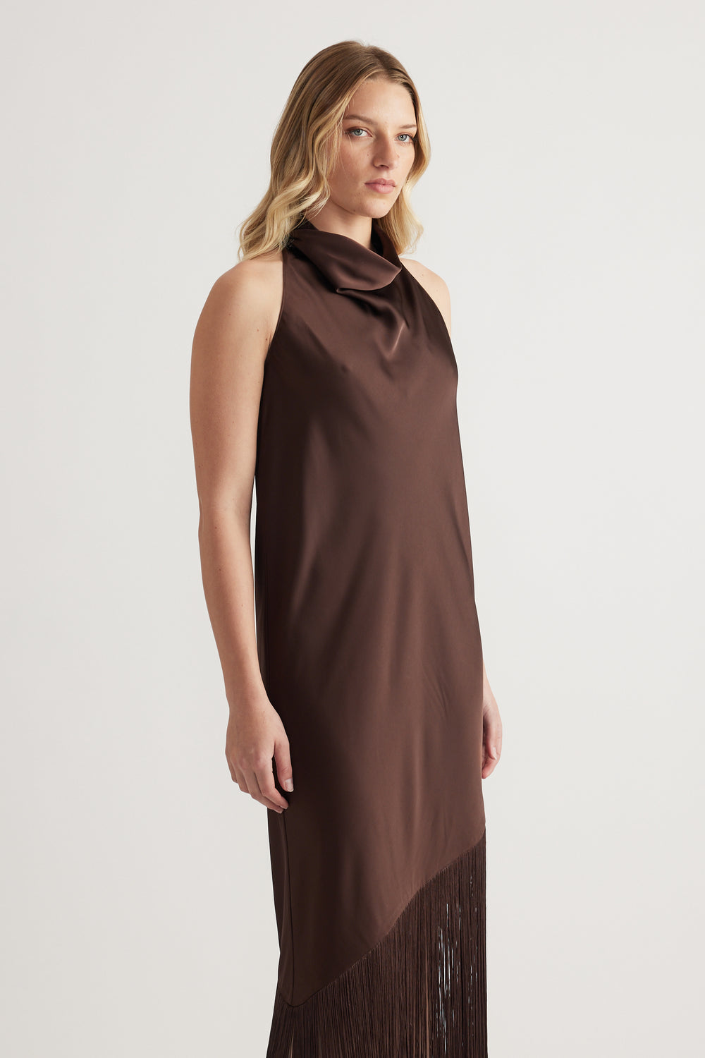 Model wearing a brown sleeveless halter maxi dress with draped finish and fringe hem