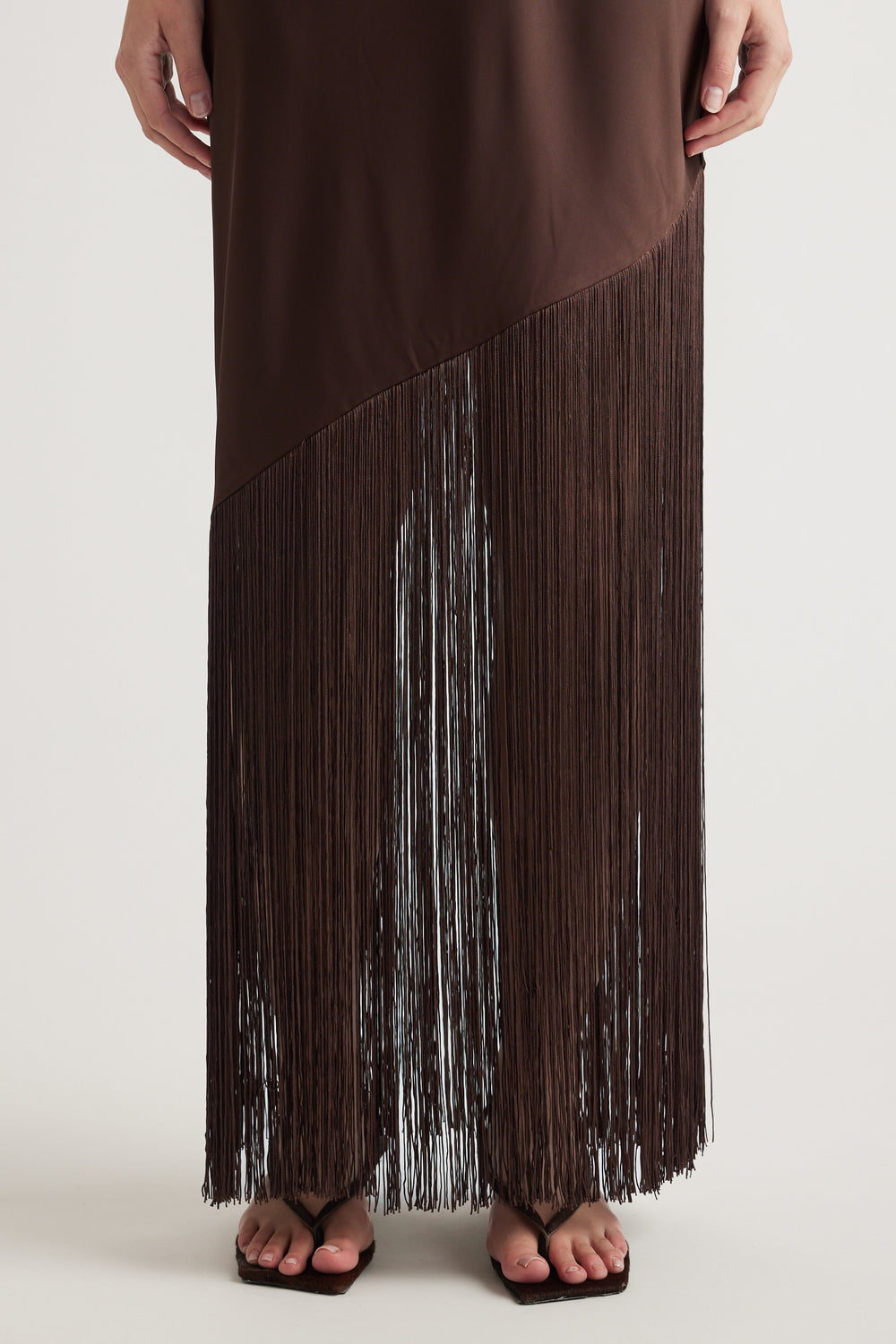 Brown maxi dress with cascading fringe hem styled with black flat sandals