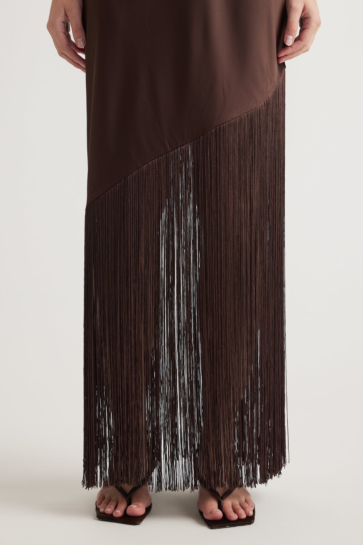 Brown maxi dress with cascading fringe hem styled with black flat sandals