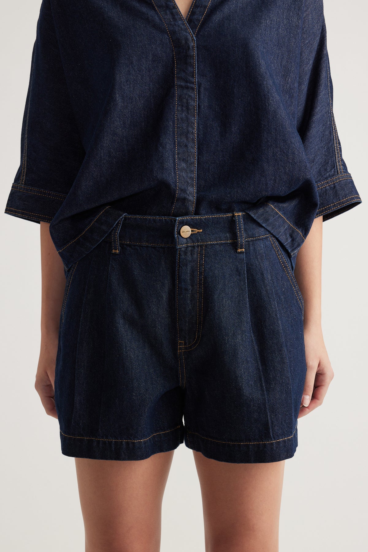 Woman wearing dark indigo high rise denim shorts with a rolled hem and matching denim top