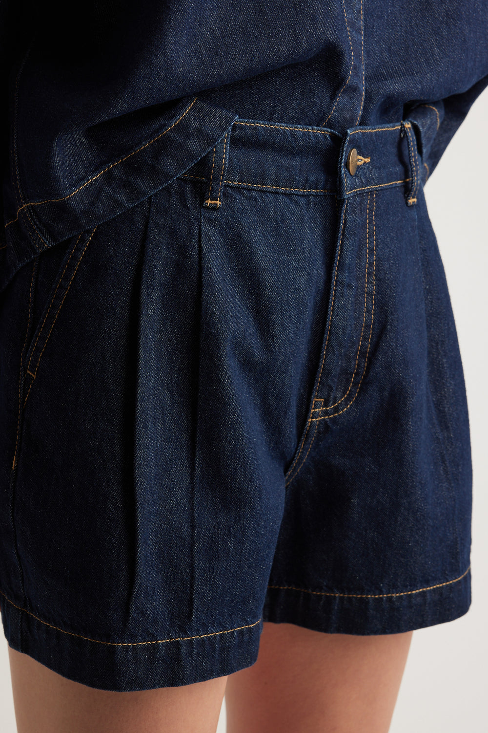 Close up of dark denim high rise shorts with front pleats and side pockets