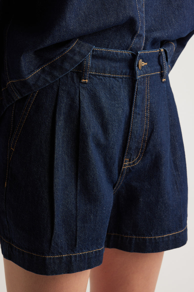 Close up of dark denim high rise shorts with front pleats and side pockets