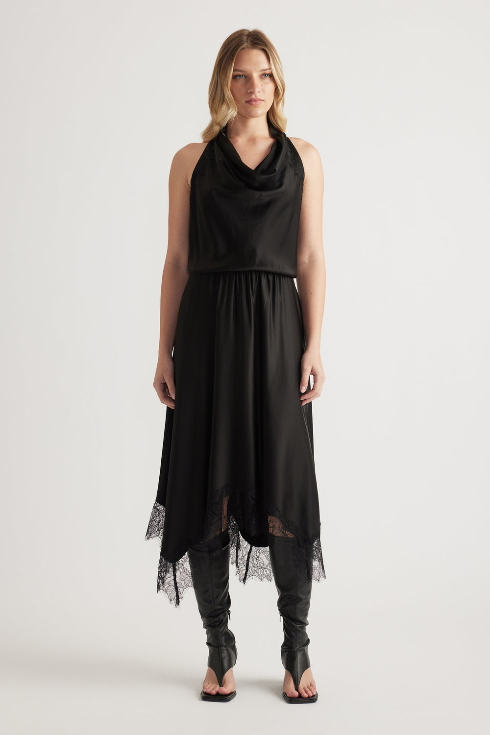 Woman wearing a black sleeveless midi dress with a draped neckline, lace hem and strappy heels