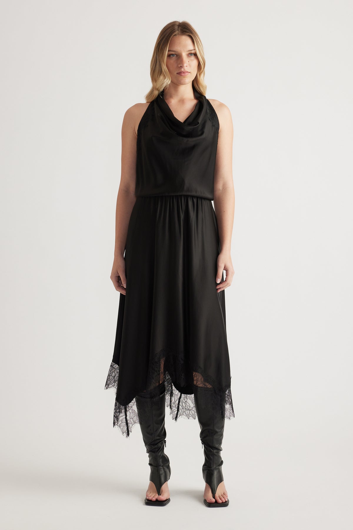 Woman wearing a black sleeveless midi dress with a draped neckline, lace hem and strappy heels