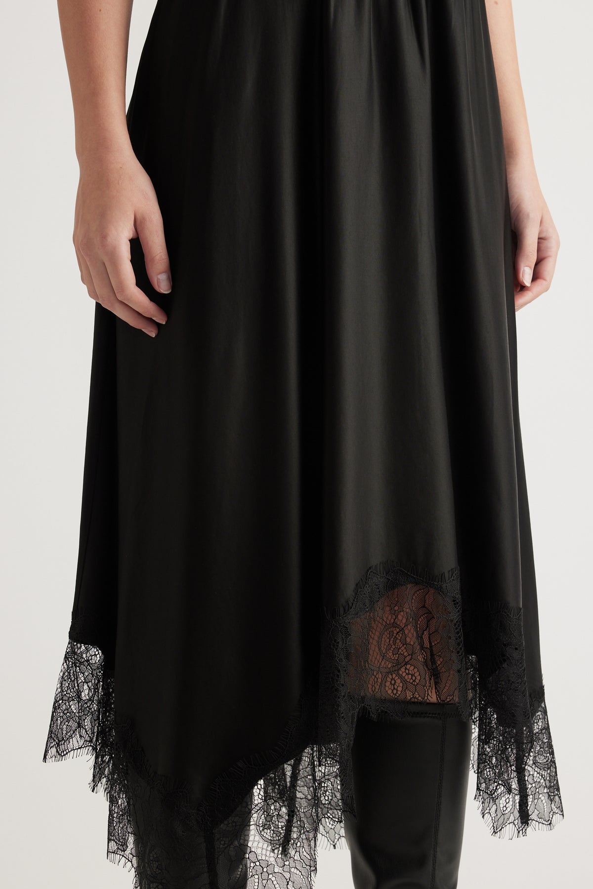 Woman wearing a black midi dress with sheer lace hem detailing and black knee-high boots