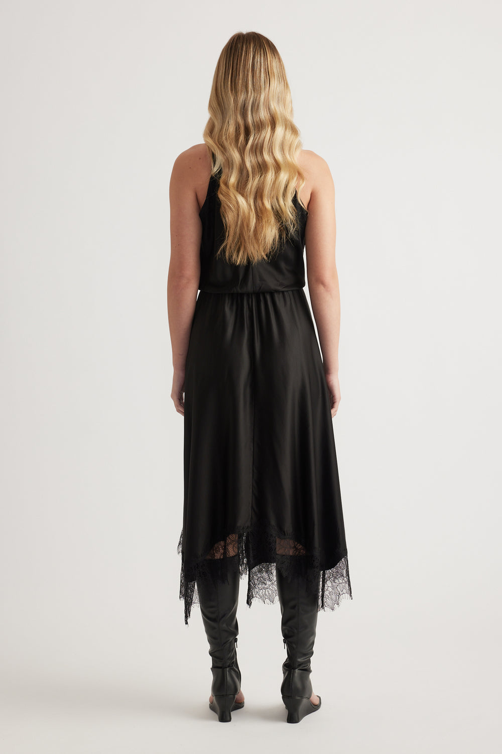 Back view of a woman in a black halter midi dress with lace hem and black boots