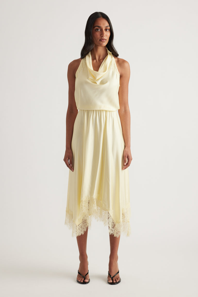 Model wearing a pale yellow halter midi dress with lace hem and black strappy sandals