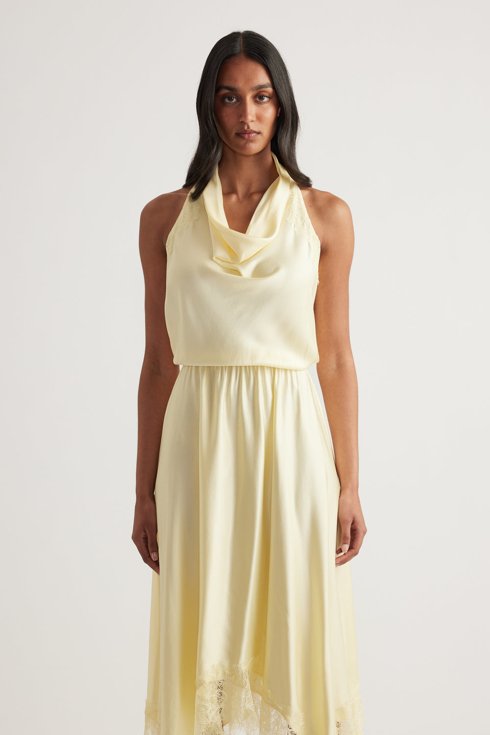 Model wearing a cream halter neck midi dress with a flowing skirt and lace hem detailing