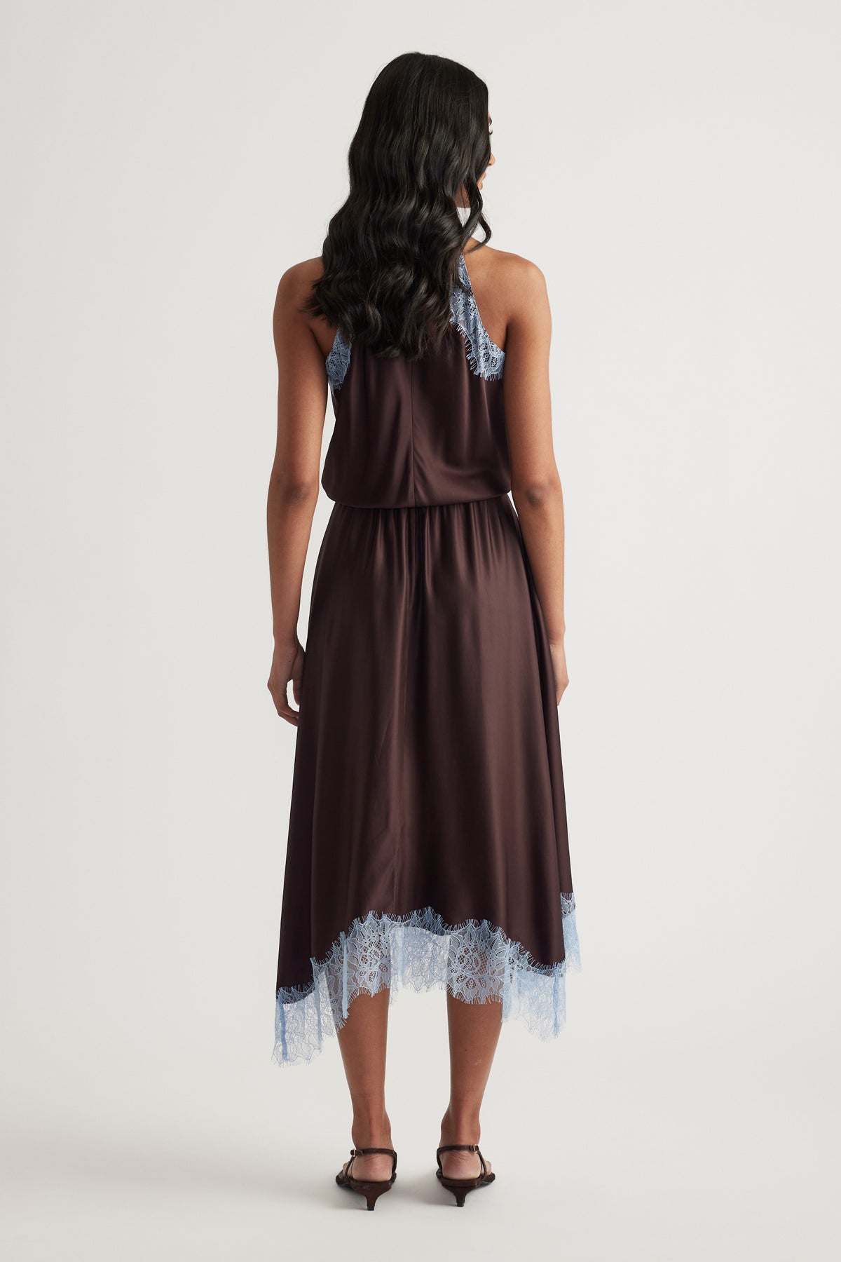 Back view of a woman wearing a chocolate brown halter midi dress with lace trim and black heels