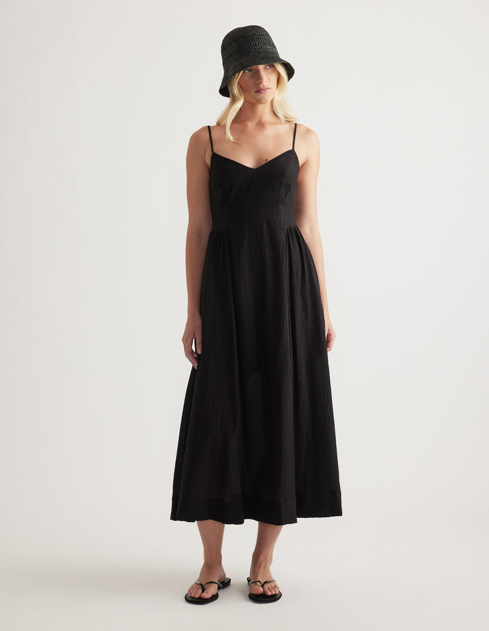 Woman wearing a black woven bucket hat with a black strappy midi dress and flat sandals