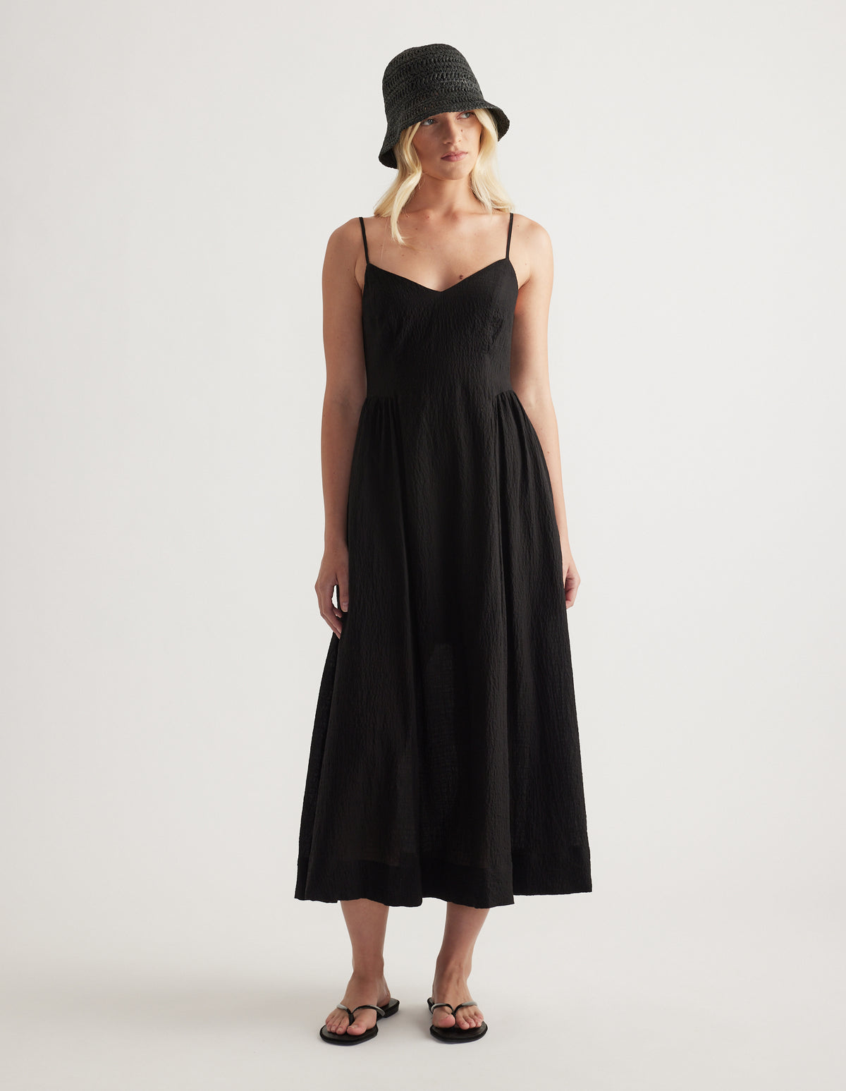 Woman wearing a black woven bucket hat with a black strappy midi dress and flat sandals