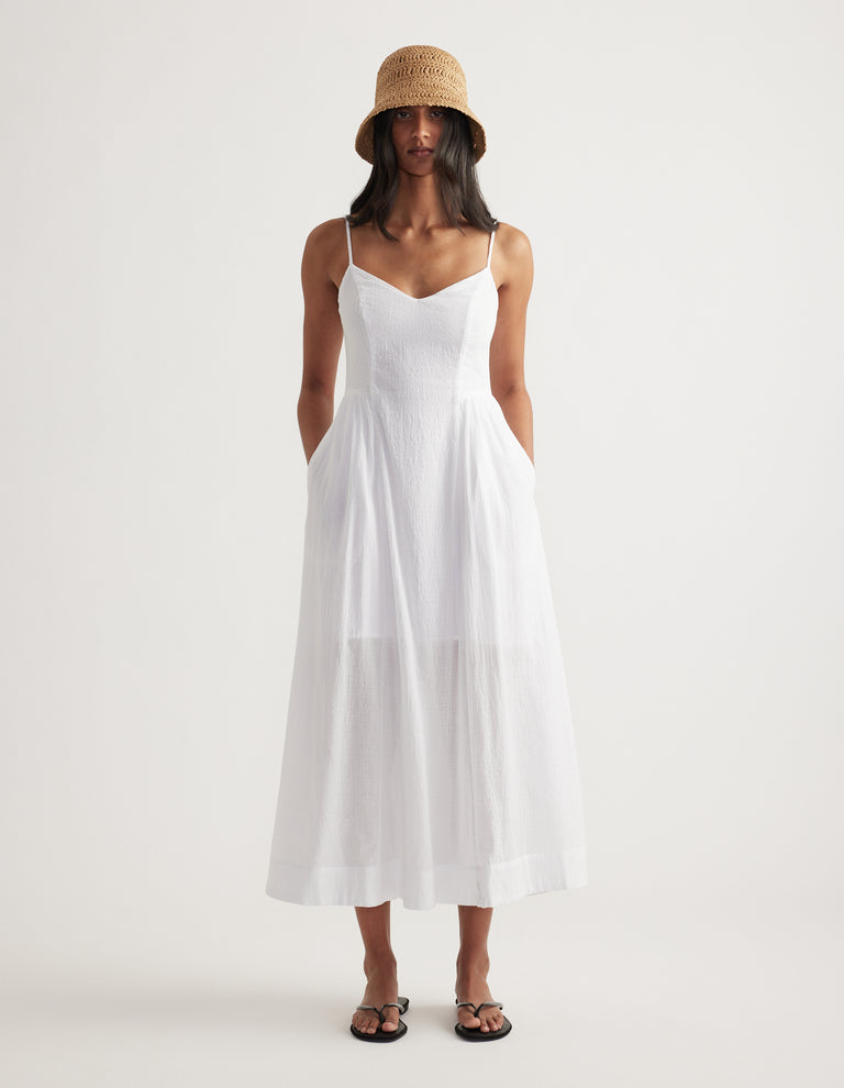 Woman wearing a lightweight tan paper weave bucket hat with a white tiered maxi dress and black sandals