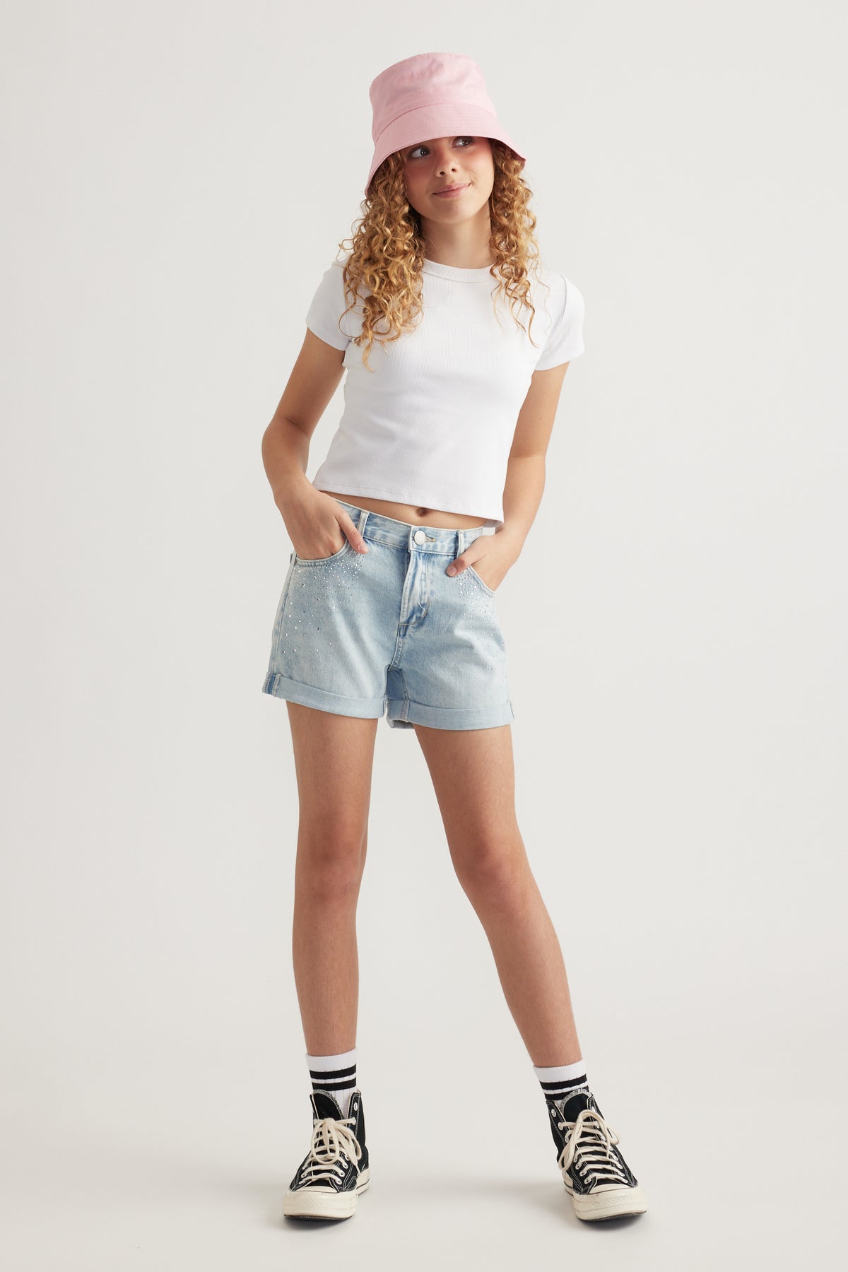 Girl wearing a pink bucket hat with a white tee, denim shorts and black high top sneakers
