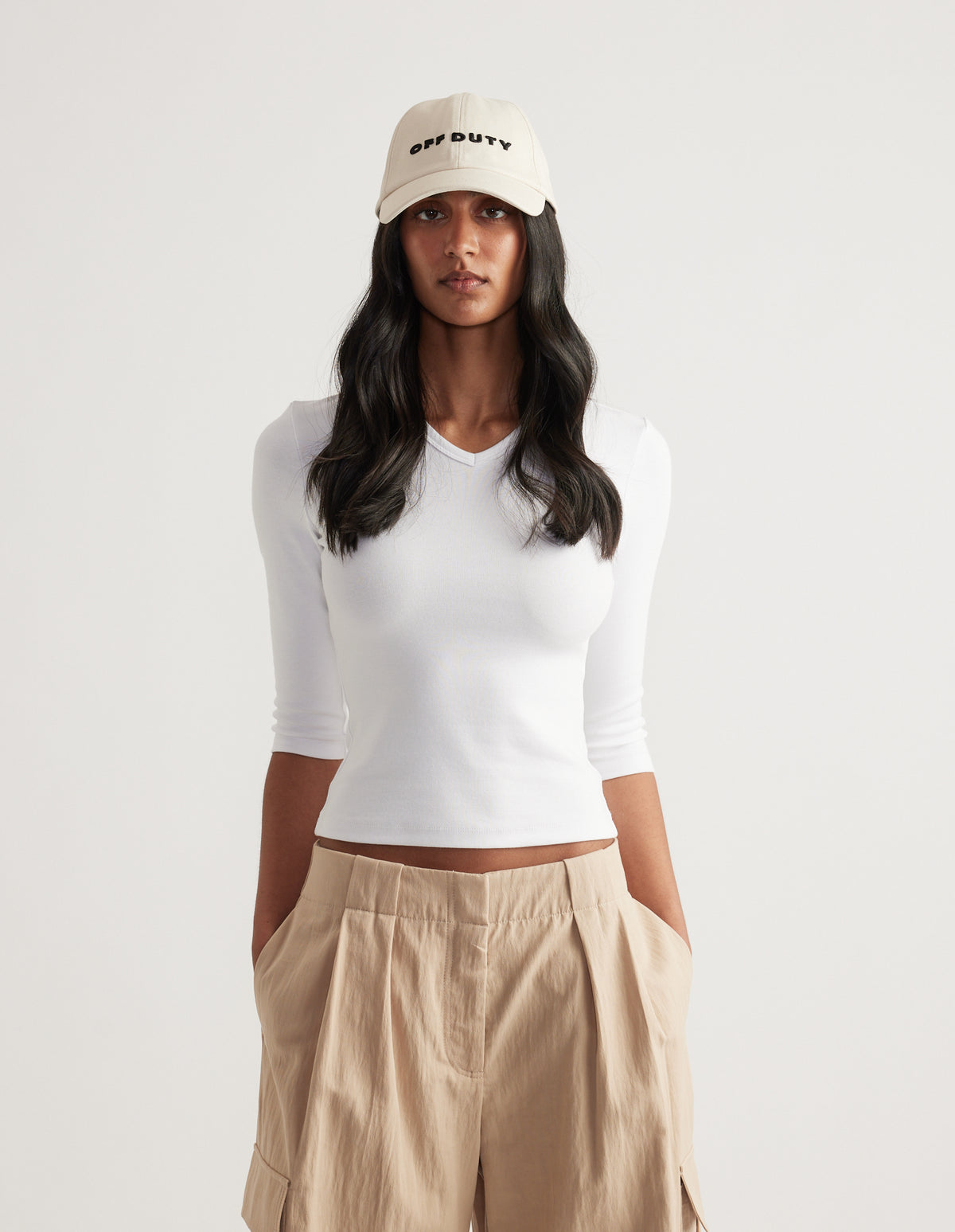 Woman wearing a cream embroidered logo baseball cap with a white long sleeve top and beige pants