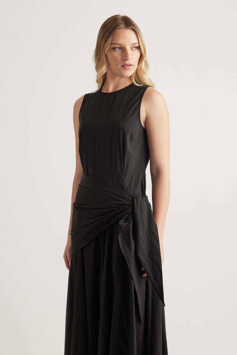Model wearing a black sleeveless midi dress with a round neckline and scarf tie waist