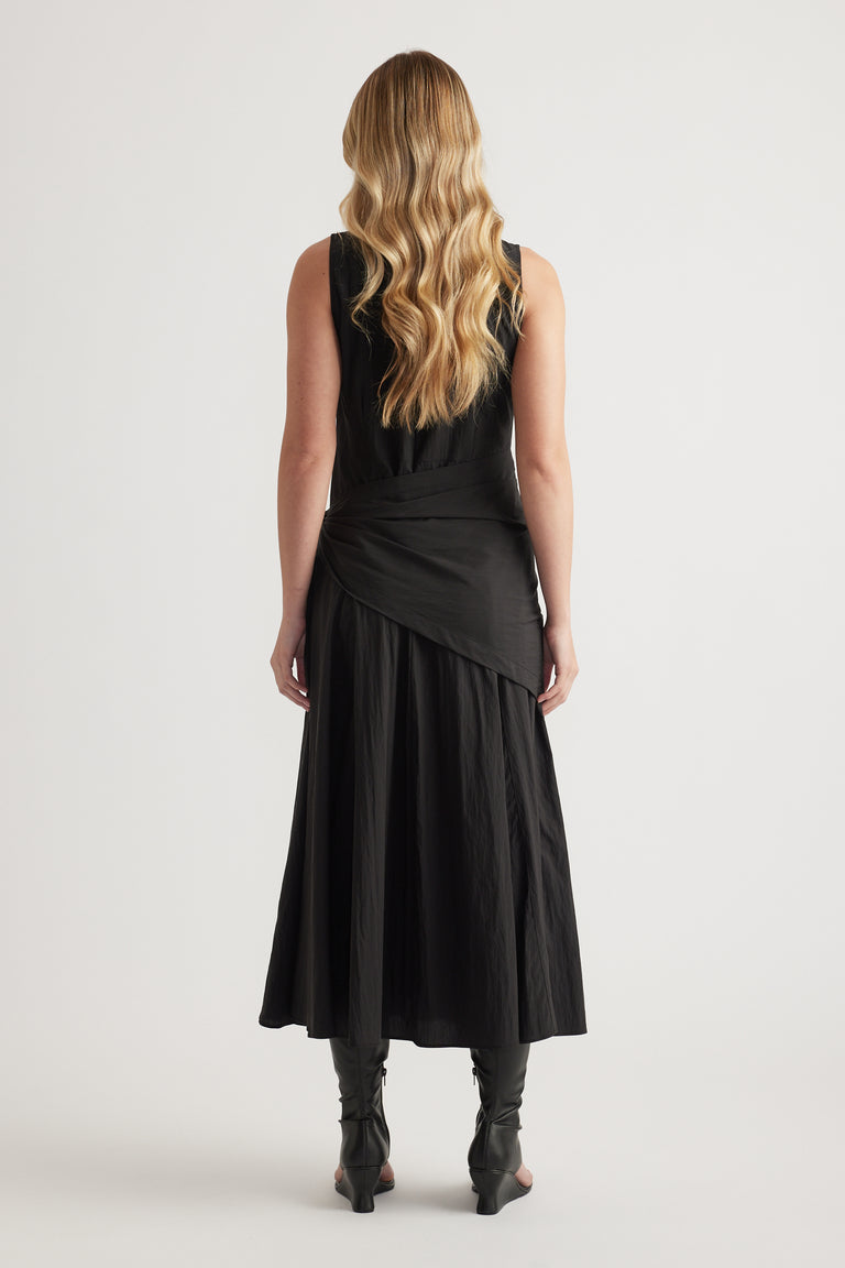 Back view of a woman wearing a black sleeveless midi dress with a draped scarf tie waist