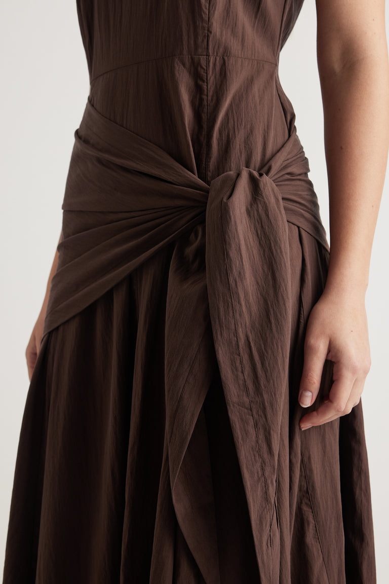 Woman wearing a brown sleeveless midi dress with a scarf tie waist and flowing column silhouette