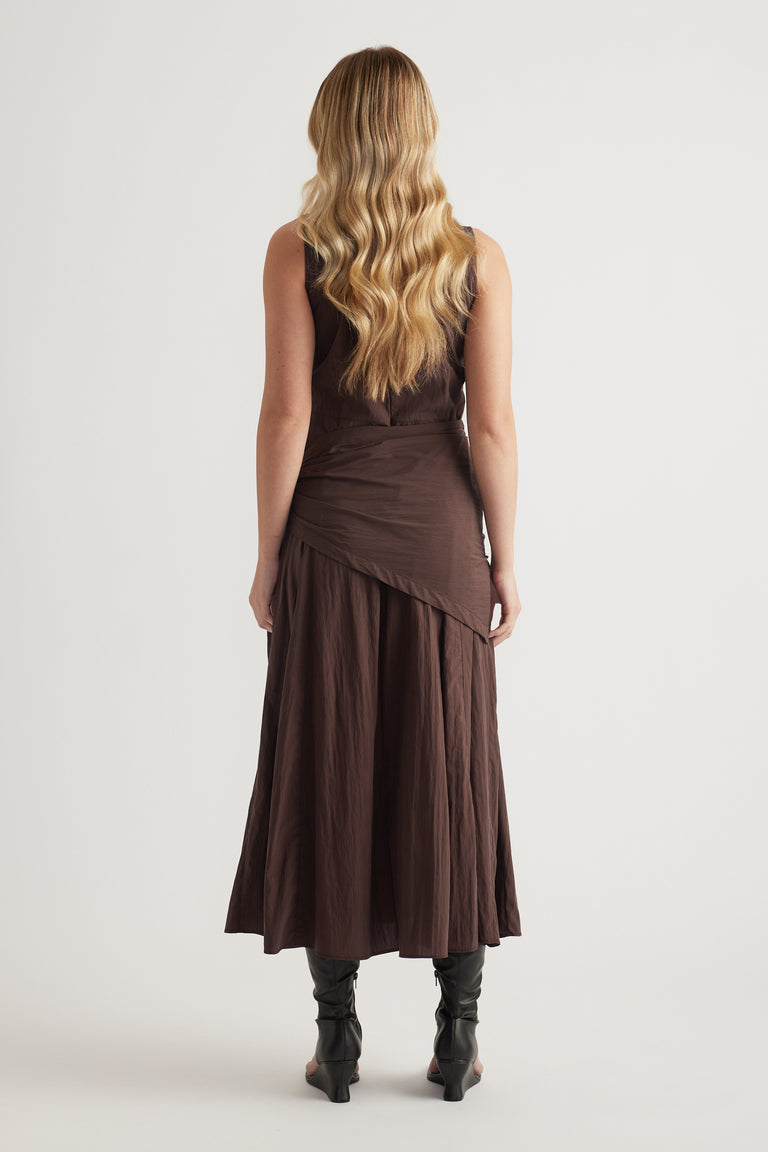 Back view of a model wearing a brown sleeveless midi dress with a scarf tie waist and flowing column silhouette