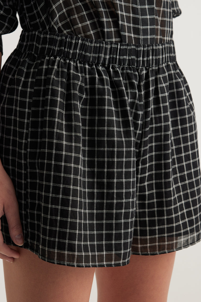 Model wearing black checked shorts with an elasticated waist and wide leg fit