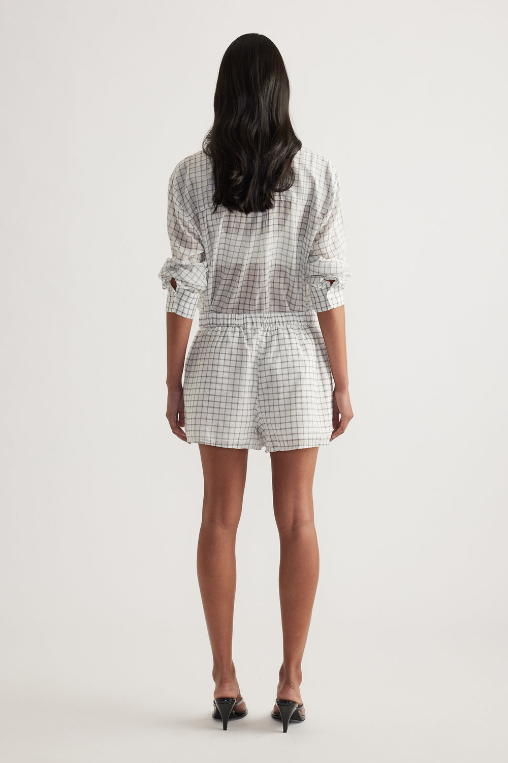 Back view of a model wearing a checked shirt with matching above-knee shorts and black heels