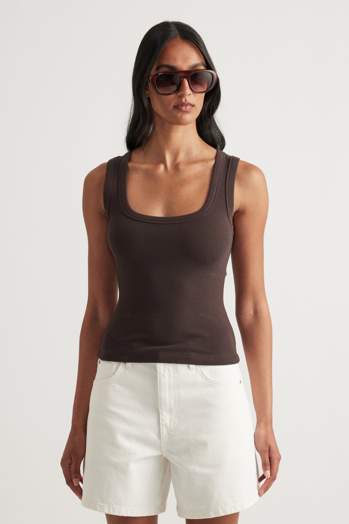 Woman wearing a brown fitted rib tank with a scoop neckline and white shorts