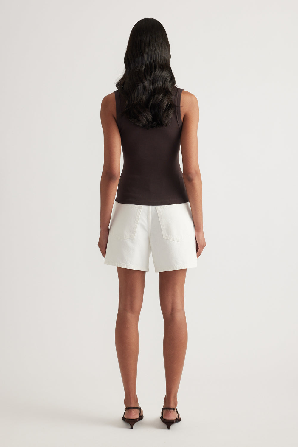 Model viewed from behind wearing a black fitted ribbed tank with white shorts and heels