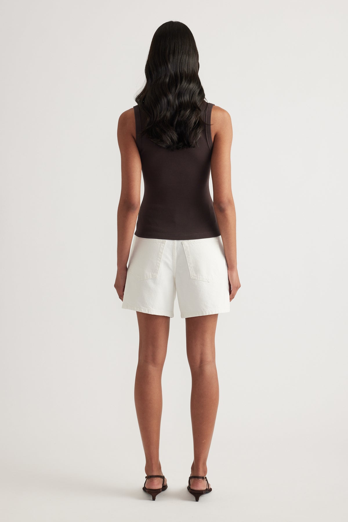 Model viewed from behind wearing a black fitted ribbed tank with white shorts and heels