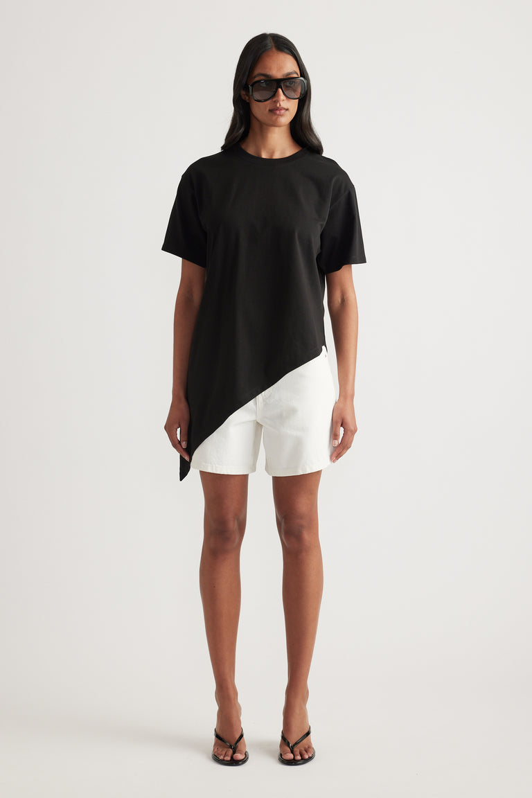 Woman wearing a black asymmetric hem tee with white shorts, sunglasses and black strappy sandals
