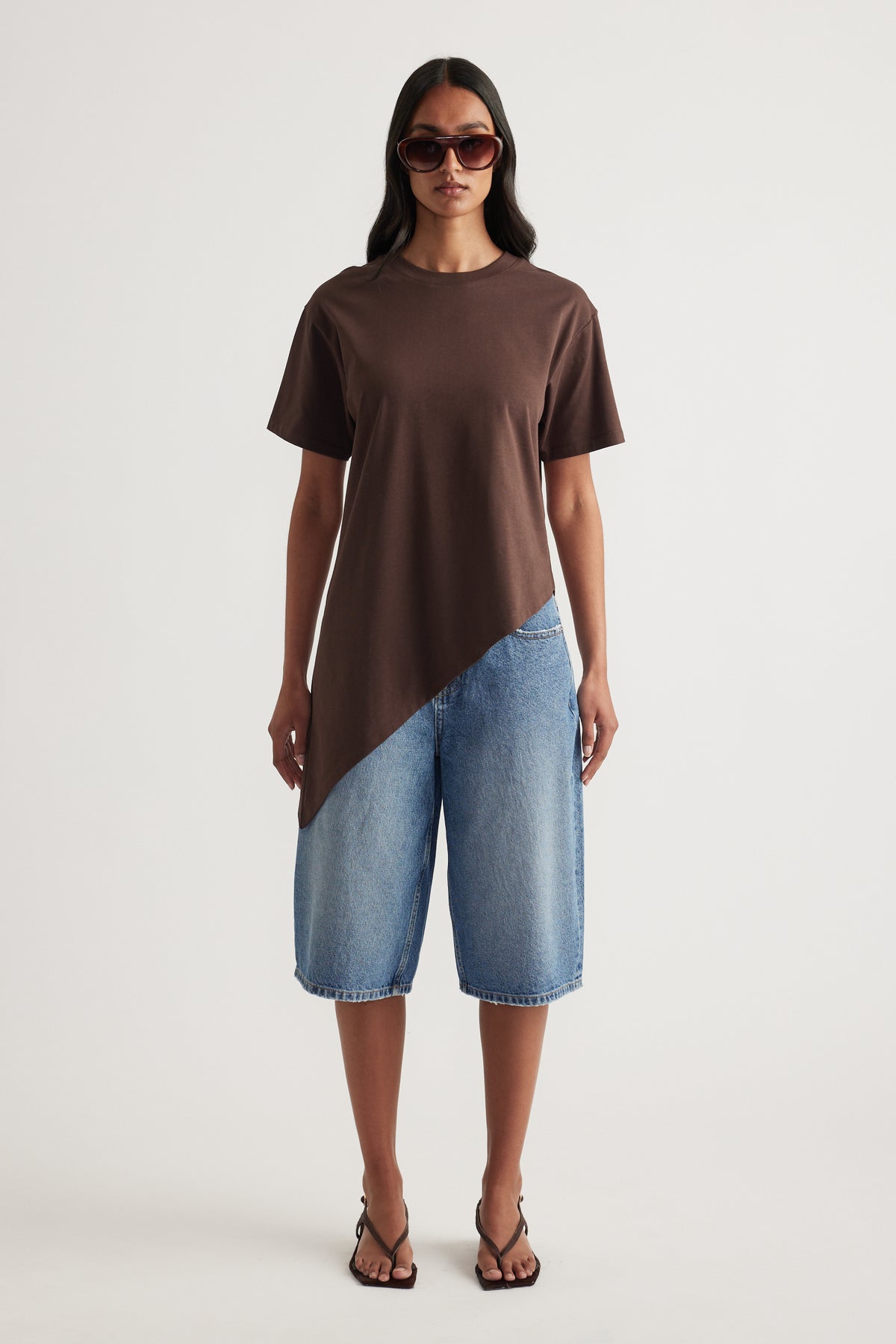Woman styling a chocolate brown asymmetric hem tee with blue denim shorts, sunglasses and strappy sandals