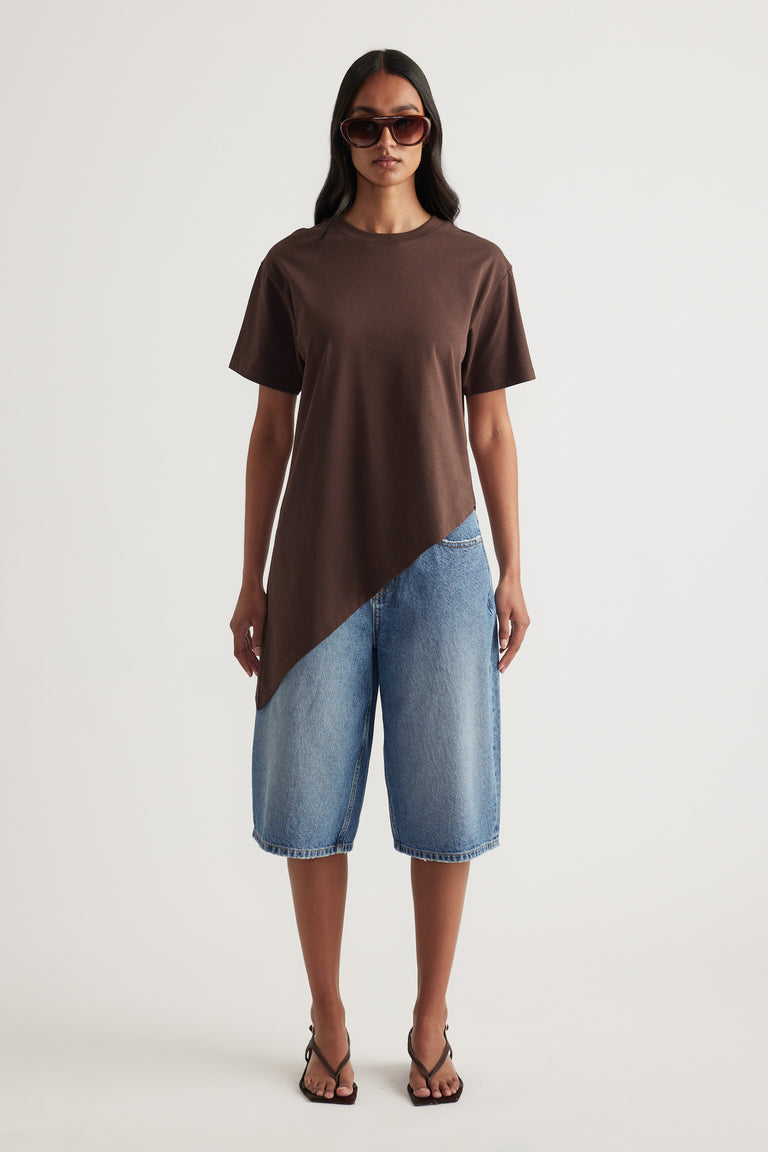 Woman styling a chocolate brown asymmetric hem tee with blue denim shorts, sunglasses and strappy sandals