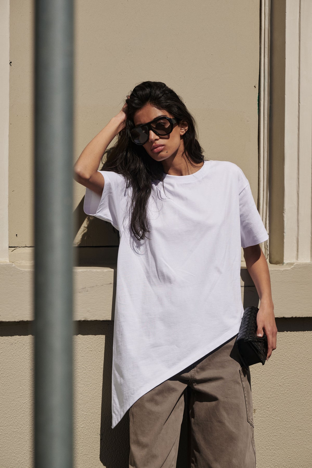 Woman wearing a white asymmetric hem tee with brown wide leg pants and black sunglasses