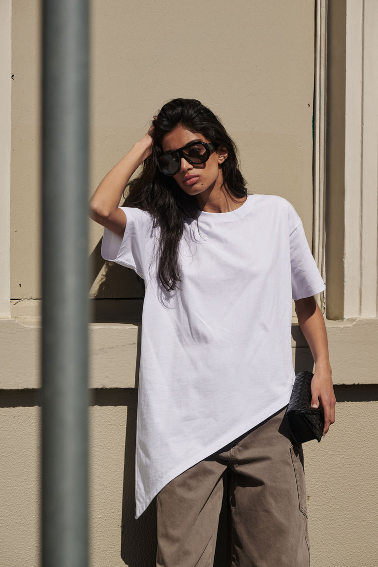 Woman wearing a white asymmetric hem tee with brown wide leg pants and black sunglasses