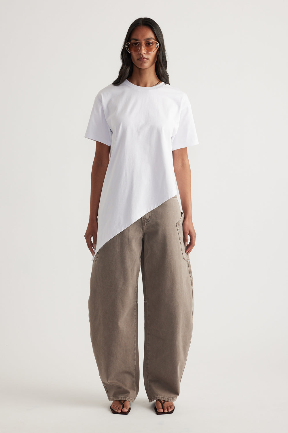 Woman wearing a white asymmetric hem tee with taupe wide leg pants, sunglasses and sandals