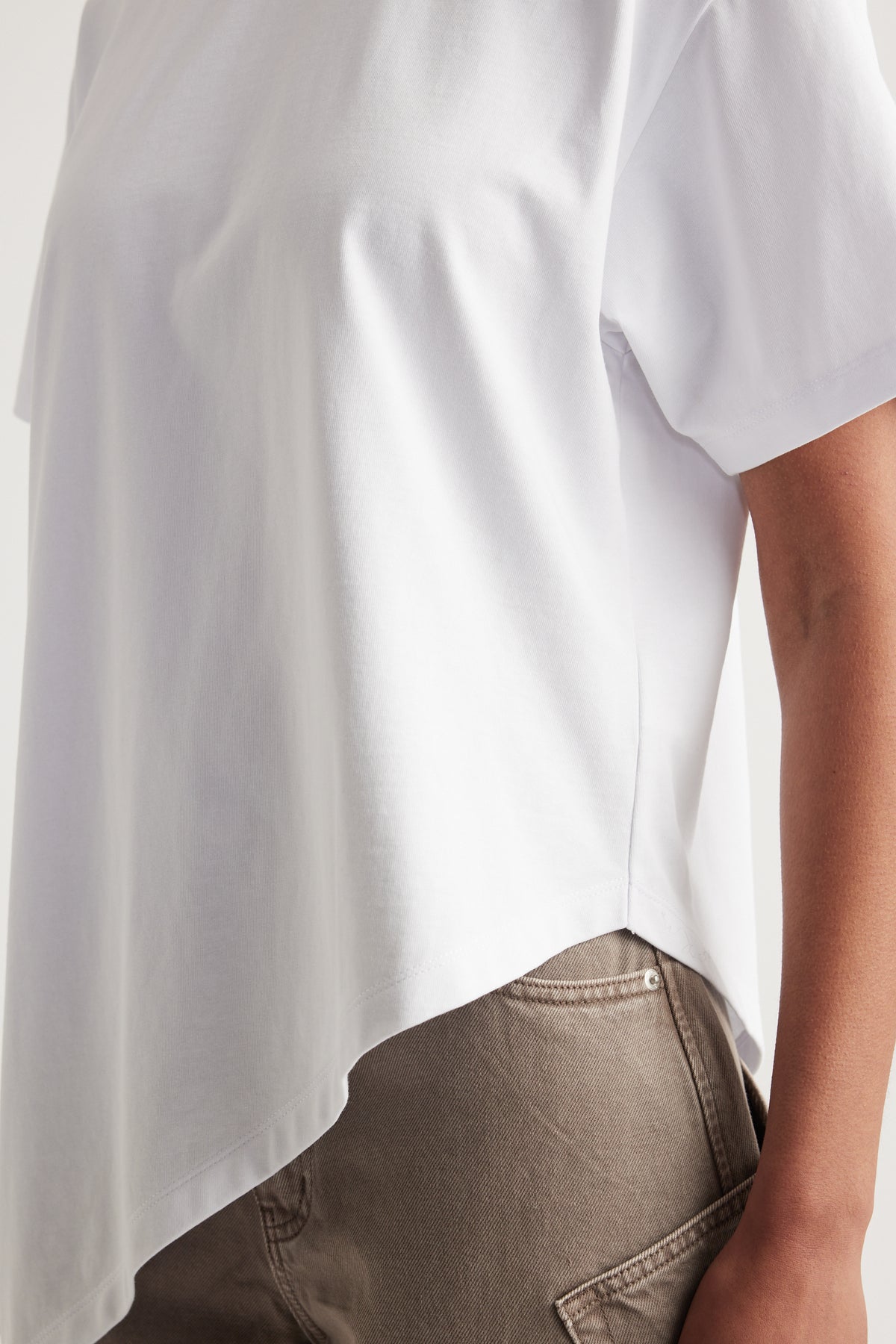 Woman wearing a white crew neck tee with an asymmetric hem and taupe jeans