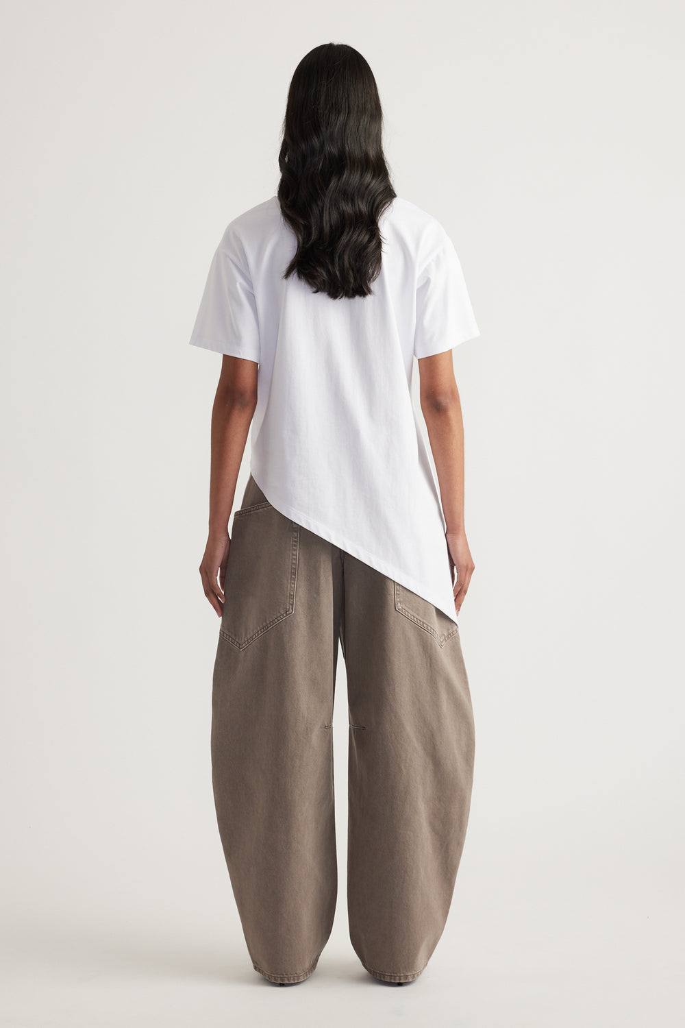 Back view of a woman wearing a white asymmetric hem tee with taupe wide leg pants