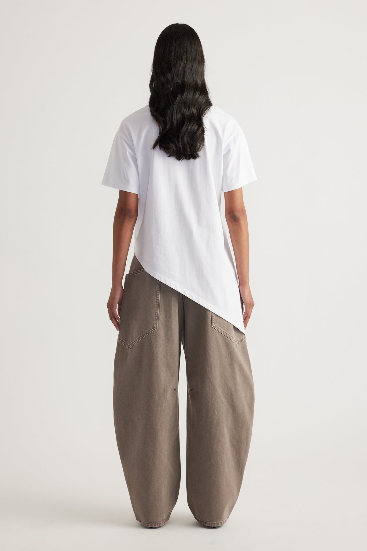 Back view of a woman wearing a white asymmetric hem tee with taupe wide leg pants