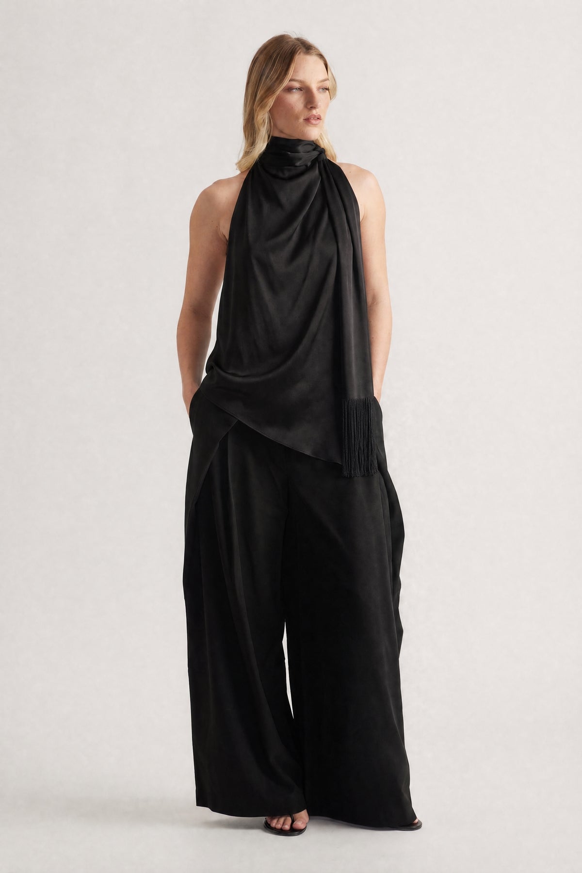 Woman wearing a black halter top with a draped fringed sash and wide leg pants