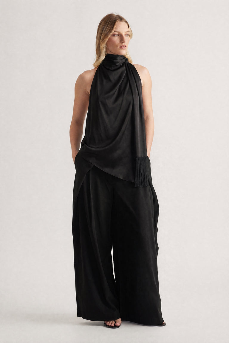 Woman wearing a black halter top with a draped fringed sash and wide leg pants
