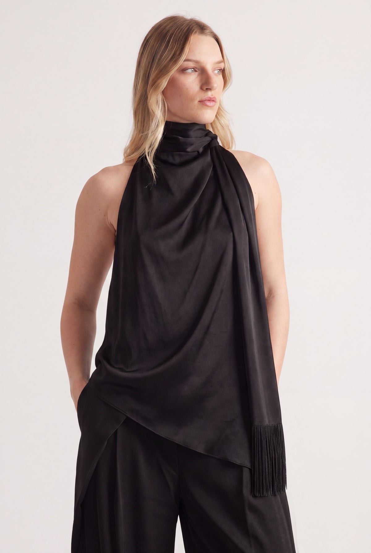 Woman wearing a black halter top with a draped fringed sash and matching pants