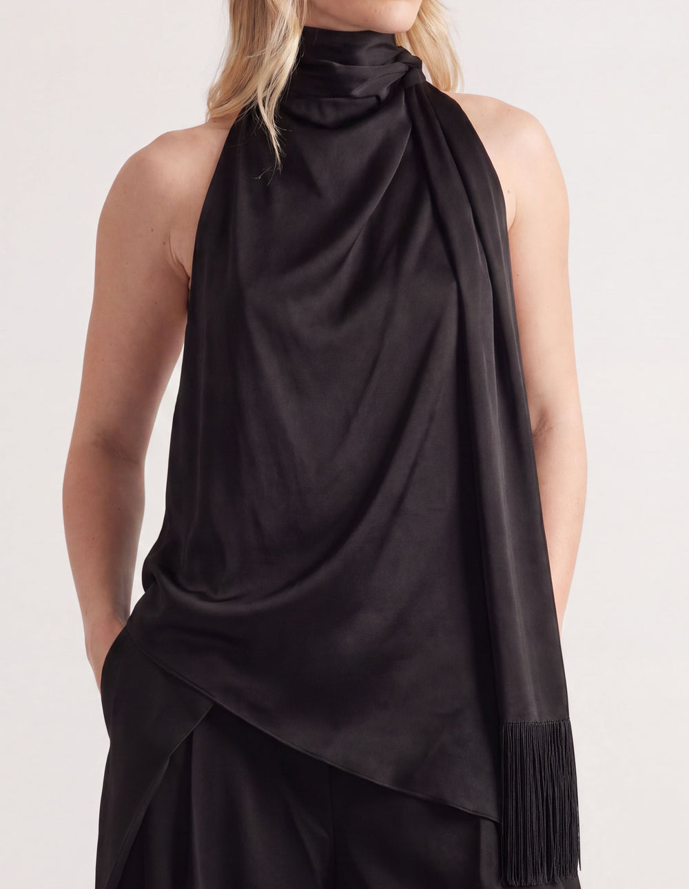 Woman wearing a black halter neck top with a draped fringed sash