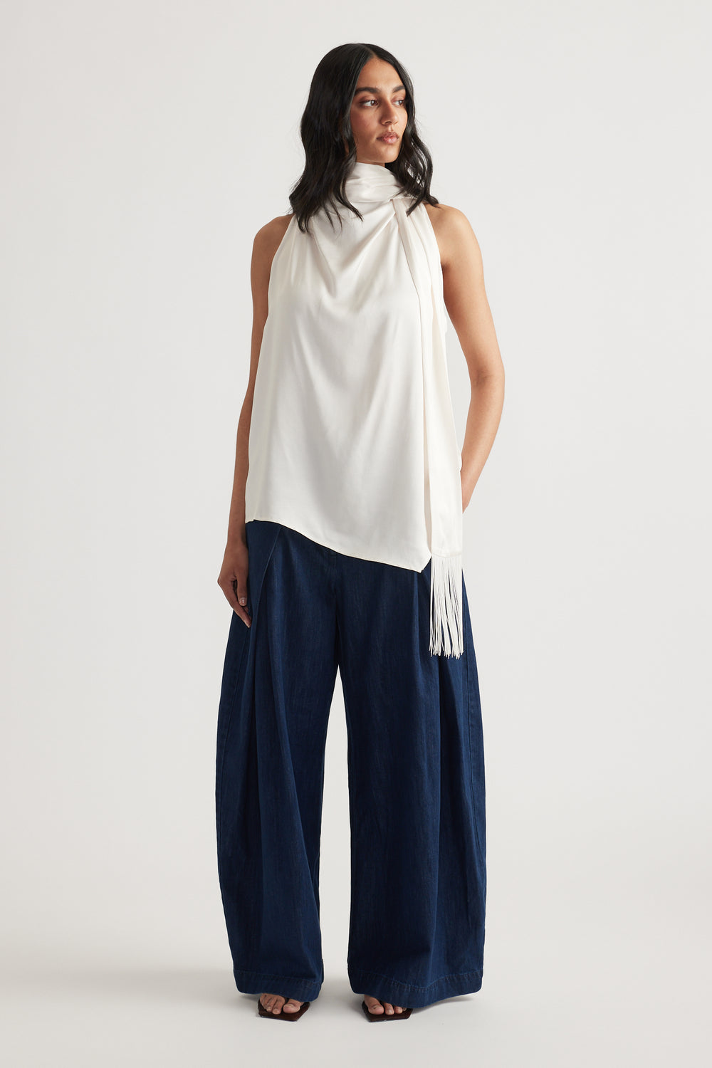 Woman wearing a white halter top with a fringed sash and navy wide leg pants