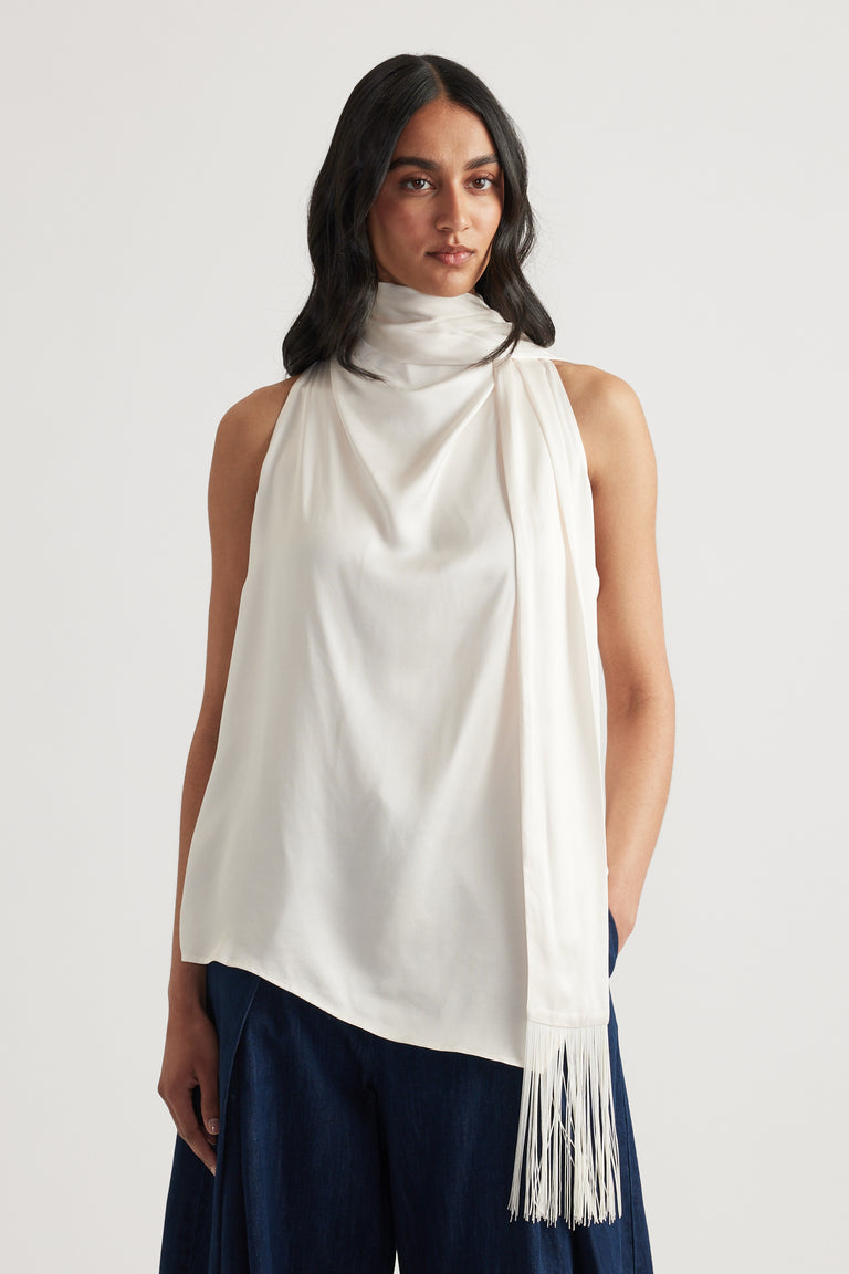 Woman wearing a white halter top with a draped fringed sash and navy pants