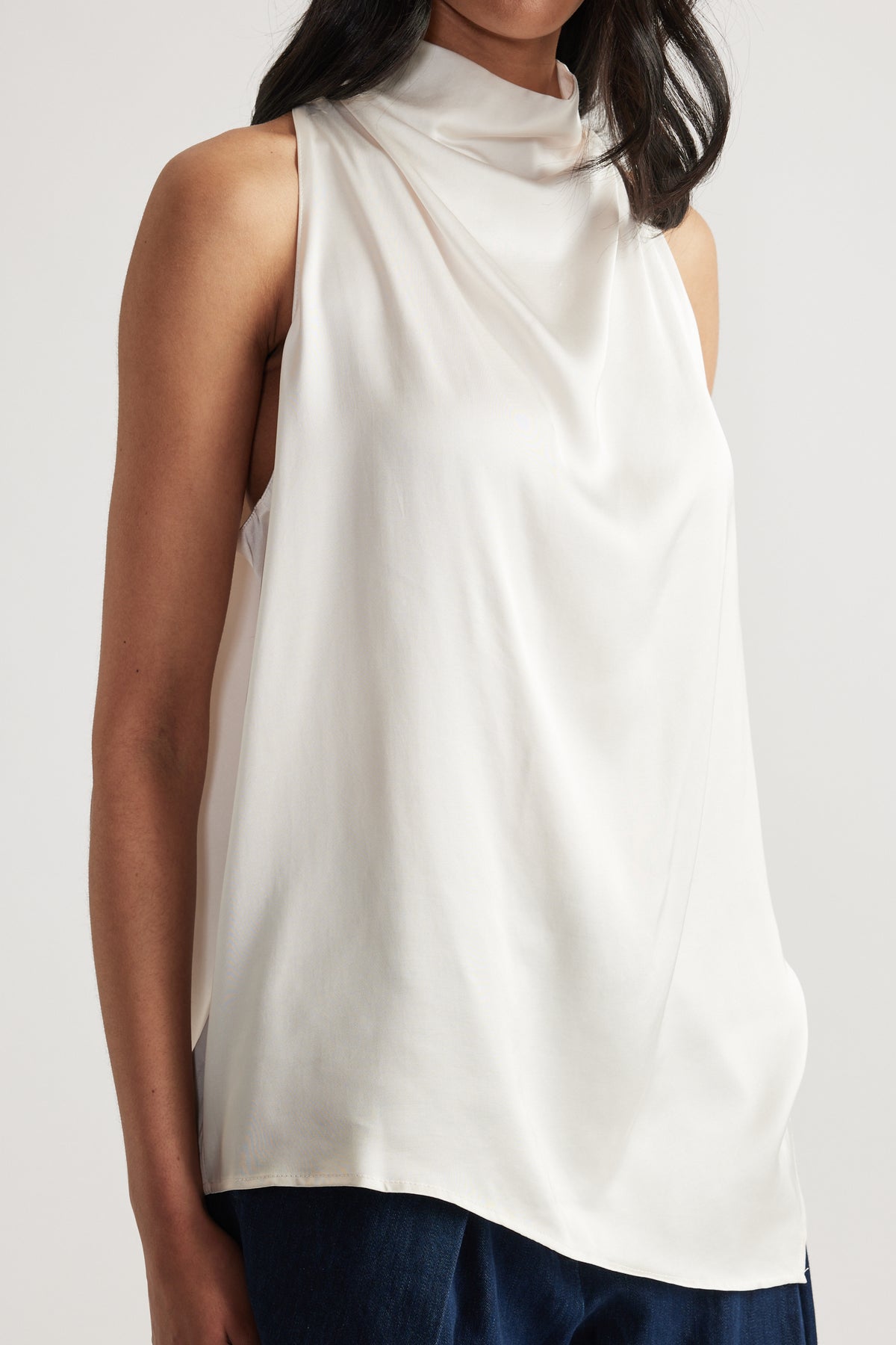 Woman wearing a white draped halter neck top with a high neckline over dark jeans