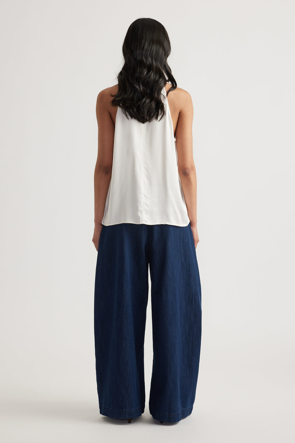 Woman seen from behind wearing a white halter top with a low scoop back and navy wide leg pants