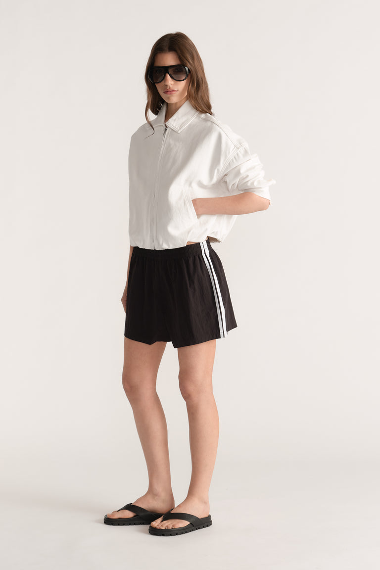 Model wearing black side stripe shorts with a white shirt and black slides