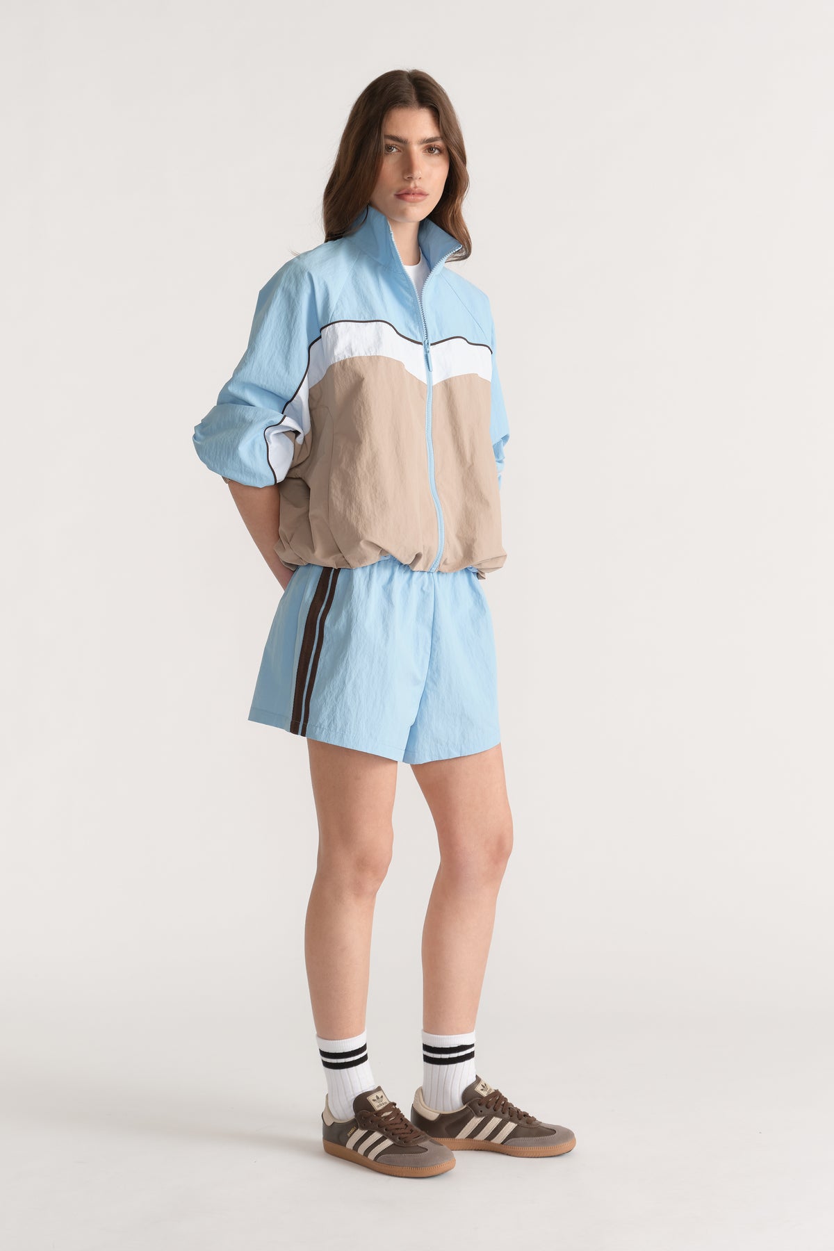 Woman wearing light blue side stripe shorts with a matching blue and beige zip jacket and sneakers