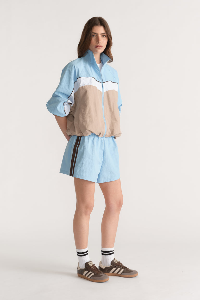 Woman wearing light blue side stripe shorts with a matching blue and beige zip jacket and sneakers