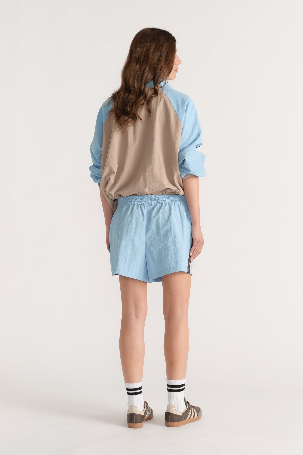 Model wearing light blue elastic waist shorts with a beige and blue jacket, striped socks and sneakers